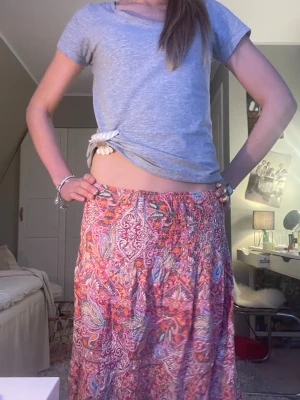 Färgglad paisleymönstrad maxikjol - Säljer en lång maxikjol med färgglatt paisleymönster i rosa, rött, orange och blått. Kjolen har en bred resår i midjan och är gjord i ett tunt, flowy material som ger en somrig vibe🌸🌼Nypris 500 kr, först till kvarn!