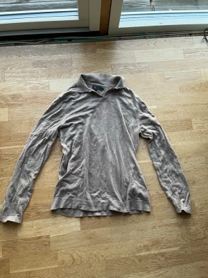 Beige långärmad tröja från Riley - Snygg beige långärmad tröja från Riley med klassisk krage och mjukt material. Perfekt för dig som gillar en stilren och enkel look. Tröjan har en avslappnad passform och diskret design utan mönster.