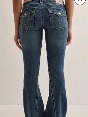 Blå bootcut jeans från True Religion - Säljer ett par blå bootcut jeans från True Religion med ikoniska kontrastsömmar och ficklock bak. Jeansen har låg midja, klassisk femficksdesign och är gjorda i stretchig denim för skön passform. Perfekta för dig som gillar en avslappnad men snygg stil. Jeansen är använda ca 5 gånger och har därför inga synliga slitningar. Stoleken kan ni se på sista bilden men de passar bra i längden för mig som är 172cm lång! Pris kan diskuteras vid snabb affär🫶🏼