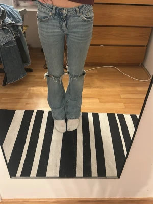 Ljusblå slitna jeans med hål - Säljer ett par ljusblå jeans med raka ben och stora slitningar vid knäna. Jeansen har klassisk femficksmodell och låg midja. Längdmodellen är short.