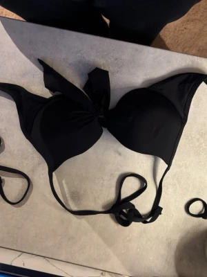Svart bikiniöverdel med knyt - Stilren panter-svart bikiniöverdel med vadderade kupor och snygg knytning framtill se till att du får perfekt passform. Klassisk trekantsmodell med tunna band som knyts i ryggen och nacken det952r enkelt att justera.