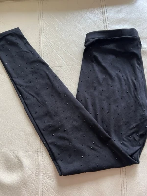 Svarta leggings med pärldetaljer - Stilrena svarta leggings med små svarta pärlor över hela tyget. Tillverkade i ett stretchigt och mjukt material som sitter tajt och bekvämt. Perfekt för dig som vill ha en extra detalj på dina leggings.