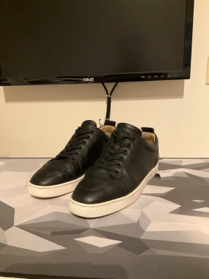 Christian Louboutin Läderskor  - Stilrena svarta sneakers i läder med klassisk låg profil och vit sula. Skorna har svarta skosnören och diskret design som passar till det mesta. Insidan är ljusbeige och materialet känns rejält och mjukt. Storlek 41 och i väldigt fint skick.
