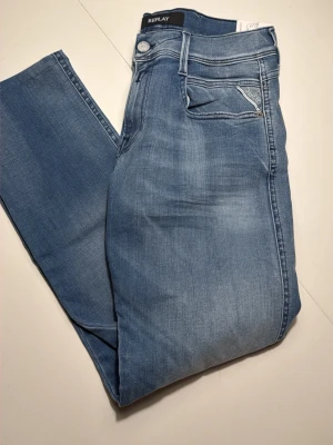 Replay Anbass ljusblå slim fit jeans - Säljer ett par ljusblå Replay Anbass jeans i slim fit med snygg tvätt och klassiska fem fickor. Jeansen är handgjorda och tillverkade i Italien, har stretchigt material och coola detaljer på fickorna. Perfekta för dig som gillar en modern och avslappnad stil.