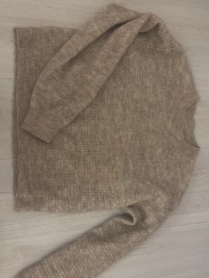 Beige stickad tröja från Lindex - Mysig beige stickad tröja från Lindex i storlek XS. Tröjan har en rak passform, ribbstickade muddar och rund hals. Perfekt för lager på lager och enkel att matcha med jeans eller kjol.