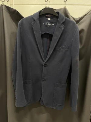 Mörkblå kavaj från Circolo 1901 - INTESSEKOLL, Stilren mörkblå kavaj från Circolo 1901 med två knappar framtill, klassisk krage. Tillverkad i mjukt bomull som ger en avslappnad men ändå dressad look. Perfekt för dig som vill ha en modern och bekväm kavaj.