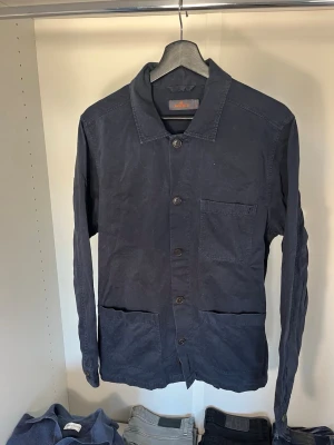 Mörkblå overshirt från Morris - Stilren mörkblå overshirt från Morris med klassisk krage och knäppning framtill. Tre praktiska fickor på framsidan och diskret logga på bröstet.  Hör gärna av dig vid frågor!