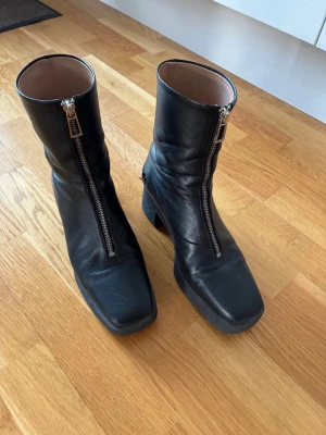 Filippa K Svarta stövletter med dragkedja - Säljer ett par svarta stövletter i skinn med grov klack och fyrkantig tå. Dragkedja framtill ger en cool look och gör dem enkla att ta på. Perfekta till höstens outfits och funkar till både jeans och kjol.