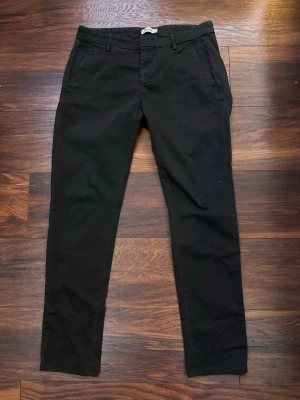 Svarta chinos från dondup  - Svarta chinos med smal passform från Dondup. Byxorna har bälteshällor och stängs med knapp och dragkedja. Storlek W32.