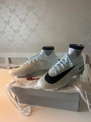 Nike Mercurial CR7 fotbollsskor - Säljer ett par Nike Mercurial CR7 fotbollsskor i vitt med svarta detaljer och högt skaft. Skorna har CR7-logga på sidan, säljer skorna då ja köpte dem i storlek 42 o en tredjedel för ja trodde dem skulle vara ”mindre o svårare få på pga strumpan men skorna var för stora för mig. Tar emot byten