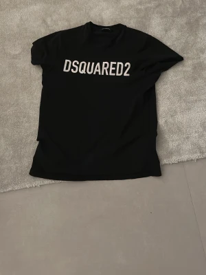  greater Svart DSQUARED2 t-shirt - Snygg svart t-shirt från DSQUARED2 med stor vit logga över bröstet. Klassisk rund halsringning och korta ärmar. Perfekt för dig som gillar stilrena och trendiga plagg med tydlig branding. Passar på storlek S ( 16 åringar)