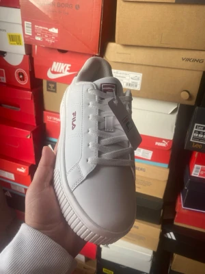 Vita Fila sneakers med chunky sula - Stilrena vita sneakers från Fila med chunky sula och klassisk låg profil. Skorna har vita skosnören, diskret Fila-logga på sidan och plösen samt ovandel i syntetmaterial. Perfekta för dig som gillar en clean och sportig look.