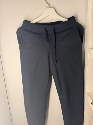 Mörkblå mjukisbyxor - Säljer ett par mörkblå mjukisbyxor med ribbad midja. Byxorna har raka ben och sidofickor, perfekta för chill dagar. Tillverkade i mjukt bomullsmaterial för maximal komfort.
