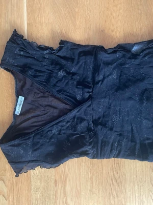   Svart topp Clockhouse - Snygg svart topp från Clockhouse med omlott-design och lätt transparent meshmaterial. Perfekt för dig som vill ha en trendig och stilren look. Använd sparsam, köpt secondhand, fint skick men tecken på användning. 