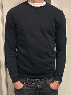 Mörkblå tjocktröja - En stilren mörkblå sweatshirt med rund halsringning och långa ärmar. Tröjan har en klassisk passform och är tillverkad i mjukt bomullsmaterial. Perfekt att matcha med jeans för en avslappnad look eller under en cardigan.