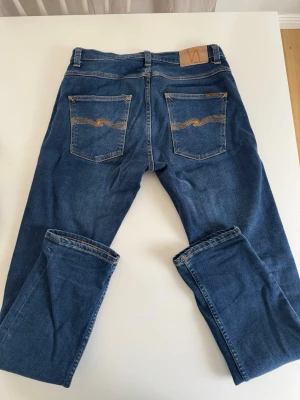 Blå jeans från Nudie Jeans - Säljer ett par klassiska blå jeans från Nudie Jeans i modellen grim trim. Tillverkade i mjuk denim som sitter skönt och passar till det mesta. Storleken är W31 L32. Använt väldigt sparsamt
