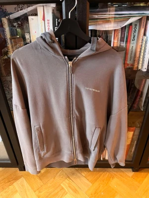 Grå zip-hoodie från Emporio Armani - Snygg grå hoodie med dragkedja från Emporio Armani. Säljer dne då den är för liten för mig och använder inte den. 