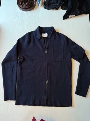 Mörkblå ziptröja från Samsøe Samsøe Guna Zip med krage - Mörkblå långärmad ziptröja med klassisk krage och bröstficka. Modell Guna Zip i storlek S. Tröjan har en rak passform och dragkedja framtill. Perfekt för lager-på-lager och enkel att matcha med olika outfits. Färgen heter Dark Sapphire