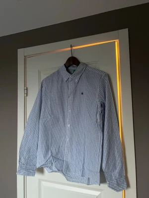 Blårutig skjorta från Benetton - Klassisk blårutig skjorta från Benetton med button-down krage och långa ärmar. Skjortan har vita knappar. Tillverkad i mjuk bomull för en bekväm känsla.