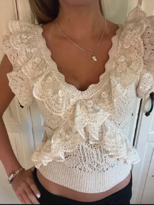 Vit spetsblus med volanger - Supersöt vit blus med v-ringning, stora volanger och spetsdetaljer. Kortärmad modell med ribbad midja och romantisk känsla. Perfekt för dig som vill ha en feminin och trendig topp till sommaren.