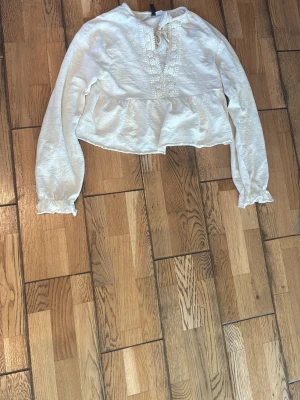 Vit blus med spetsdetaljer - Söt vit blus med fina detaljer och knyte upp till. Den är något kroppad. Blusen är i storlek xs från hm. Den är i fint skick och säljs pågrund av att den ej kommer till användning. 