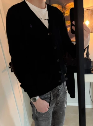 Svart cardigan från Ralph Lauren - Stilren svart cardigan från Ralph Lauren med knäppning framtill och två fickor. Liten broderad logga på bröstet. Perfekt att slänga över en t-shirt för en avslappnad men snygg look.skicket ligger på 9/10, priset är inte hugget i sten!💎✅ nypris ligger på ca 2700! Perfekt för en vanlig dag eller en lite schystare tillställning😇