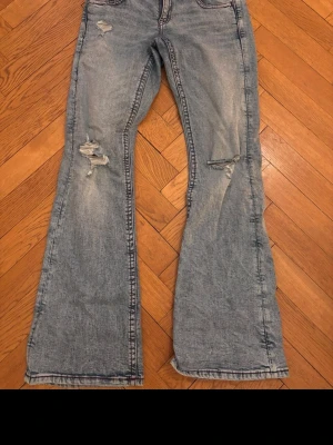 Ljusblå bootcut jeans med slitningar - Säljer ett par ljusblå bootcut jeans från Gina Tricot med slitna detaljer på benen och fem klassiska fickor. Jeansen har en avslappnad passform och markerade sömmar. Perfekta för en trendig och avslappnad look. Frågor?? Kontaka mig