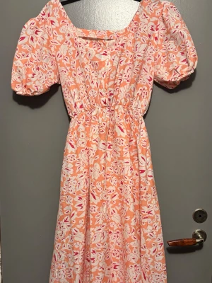 Blommig långklänning med puffärm - Superfin långklänning med blommigt mönster i rosa, vitt och rött/orange. Klänningen har puffärmar, markerad midja och rundad halsringning. 