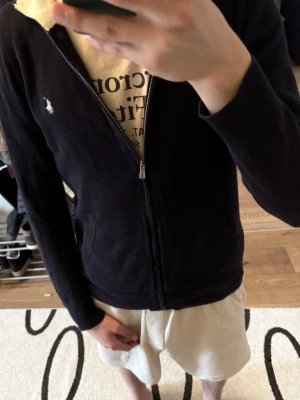 Ralph Lauren ziptröja - Snygg marinblå ziptröja från Polo Ralph Lauren. Tröjan har dragkedja framtill, två fickor och är tillverkad i 100% bomull. Perfekt för en avslappnad och stilren look.
