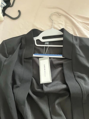 Svart kavaj från SHEIN - Stilren svart kavaj från SHEIN med klassisk krage och öppen front. Kavajen har en rak passform och är tillverkad i ett lätt material som ger en snygg och modern look. Perfekt för att lyfta vilken outfit som helst.