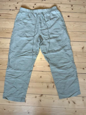 Ljusbeige vida linnebyxor - Säljer ett par ljusbeige linnebyxor med avslappnad passform och resår i midjan. Byxorna har raka ben och är tillverkade i ett tunt, luftigt linnematerial som passar perfekt för varma dagar. Inga synliga fickor eller detaljer. Perfekta för en chill och stilren look. OBS! Ankellängd. 