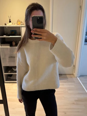 Vit stickad tröja med rund hals - Säljer en enkel och snygg vit stickad tröja med rund hals och långa ärmar. Tröjan har en rak passform och ribbstickade muddar vid ärmslut och nederkant. 