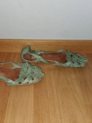 Gröna flätade sandaler i läder - Snygga gröna sandaler med flätad design och öppen tå. Tillverkade i mjukt läder med justerbart spänne vid ankeln. Perfekta för varma dagar och ger en avslappnad men trendig look.