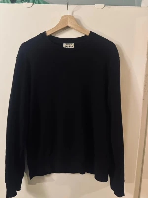 Svart stickad tröja från Acne Studios - Klassisk svart stickad tröja från Acne Studios med rund halsringning och långa ärmar. Tröjan har en enkel och stilren design med ribbade muddar vid ärmslut och nederkant. Perfekt basplagg för en clean look.