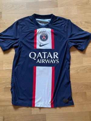 PSG Neymar Jr matchtröja blå - Säljer en blå Paris Saint-Germain matchtröja från Nike med Neymar Jr och nummer 10 på ryggen. Tröjan har vita och röda detaljer, PSG-logga på bröstet och Qatar Airways som sponsortryck. Tillverkad i lätt och ventilerande material, perfekt för fotbollsträning.