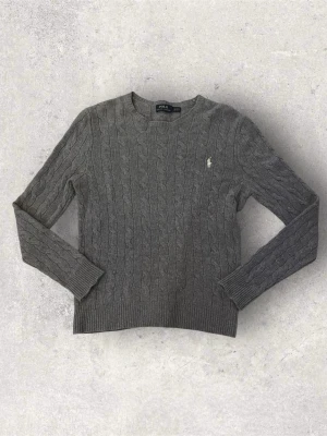 Ralph Lauren kabelstickad tröja grå – L barnstorlek (sitter som XS) - Klassisk kabelstickad tröja från Ralph Lauren. Märkt L i barnstorlek, men sitter mer som XS i damstorlek.  Färg: Grå Storlek: L (barnstorlek) – passar ungefär XS dam Skick: Mycket bra skick, men det finns ett hål på sidan av armen (se bild). I övrigt är tröjan fin.  Stilren och tidlös modell med broderad logga på bröstet. Perfekt till vardag eller höst/vinter.  Skriv gärna om du har frågor eller vill ha fler bilder! 😊
