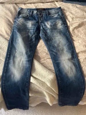 Blåa jeans från Dan paisi - (Storlek på sist bild) Säljer ett par blåa jeans från Dan paiI  med snyggt slitna detaljer och ljusa partier framtill och baktill. Klassisk femficksmodell med raka ben och normal midja. 