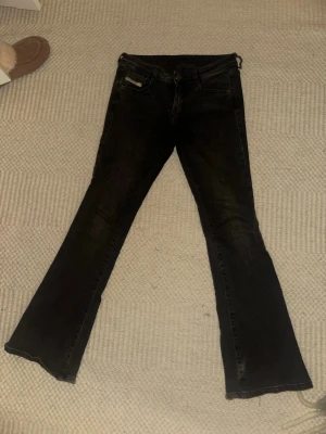 Svarta bootcut jeans från Diesel - Säljer ett par svarta bootcut jeans från Diesel med klassisk femficksdesign och råa kanter längst ner. Jeansen har en snygg passform och är tillverkade i denim med stretch för extra komfort.