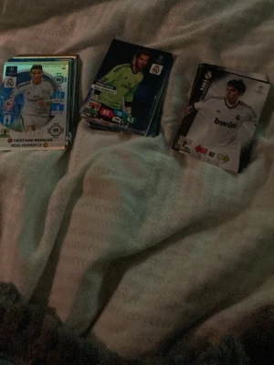 Samling fotbollskort real Madrid  - Säljer en samling fotbollskort med olika spelare och lag, bland annat Real Madrid. Korten har färgstarka tryck och är gjorda av glansigt papper. Perfekt för dig som gillar att samla på sportkort eller vill byta med vänner.