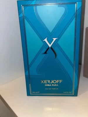 Xerjoff Erba Pura Eau de Parfum - Xerjoff Erba Pura Eau de Parfum i en snygg turkosblå kartong med gulddetaljer. Förpackningen har en stor X-logga och rymmer 100 ml. Lyxig och modern design som sticker ut på parfymhyllan.
