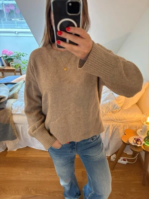 Beige oversized stickad tröja - Mysig beige stickad tröja med avslappnad passform och breda ribbade muddar vid ärmslut och nederkant. Tröjan har rund halsringning och är perfekt för lager på lager. Passar till jeans eller kjol för en chill look.