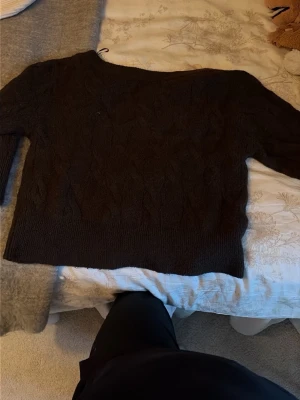 Mörkbrun stickad tröja Gina Tricot - Mysig mörkbrun stickad tröja från Gina Tricot med diskret mönsterstickning. Tröjan har långa ärmar och bred ribbad mudd vid nederkant och ärmslut. Perfekt för kyliga dagar och enkel att matcha med jeans eller kjol.