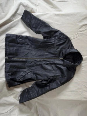 Svart lång jacka i äkta läder - Svart lång skinnjacka med rak passform i äkta läder med dragkedja framtill. Köpt Secondhand, okänt märke. 