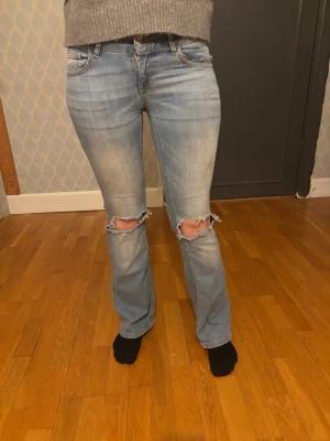 Ljusblå slitna bootcut jeans - Ljusblå bootcut jeans med slitningar och hål vid knäna. Jeansen har klassisk femficksdesign och snygga detaljer på bakfickorna. Perfekt för en avslappnad och trendig look.