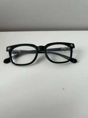 Chrome hearts glasögon - Snygga svarta glasögon med rektangulära bågar och små silvriga stjärndetaljer i hörnen. Bågarna är i plast och har en klassisk, stilren look som passar till många stilar.