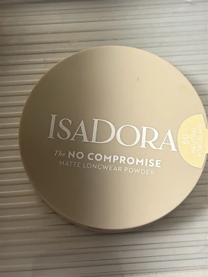 IsaDora Matte Longwear Powder 60 - IsaDora The No Compromise Matte Longwear Powder i färgen 60 Neutral Porcelain. Kompakt puder i rund, beige förpackning med silvrig text. Ger en matt finish och lång hållbarhet, perfekt för en naturlig look.
