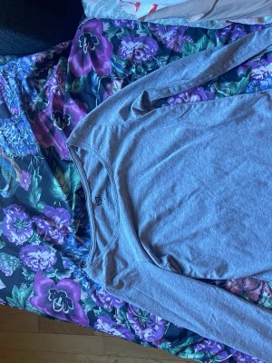 Grå långärmad basic tröja - En enkel och stilren grå långärmad tröja i mjukt bomullsmaterial. Tröjan har rund halsringning och en slim fit passform som funkar till det mesta. Perfekt att ha som basplagg i garderoben, Från lager 157.