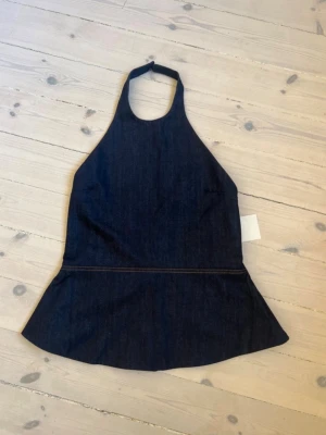 Mörkblå denim halterneck topp - Trendig mörkblå halterneck topp från Sisters Point i denim. Toppen har en figurnära passform upptill, markerad midja och utställd nederdel. Stängs med dragkedja bak och har en snygg söm som markerar midjan. Perfekt för en cool och modern look.