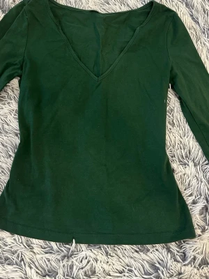 Mörkgrön långärmad v-ringad topp - En enkel och stilren mörkgrön långärmad topp med v-ringning. Tillverkad i mjuk bomull som känns skön mot huden. Perfekt att matcha med jeans eller kjol för en clean look.