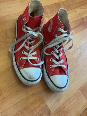 Röda Converse All Star Highs - Klassiska röda Converse All Star high-top sneakers med vita gummisulor och tåhättor. Skorna har vita snören och silverfärgade öljetter. Tillverkade i canvas med den ikoniska loggan på sidan. Perfekta för en cool och avslappnad stil. Obs inte tvättad innan bild tagits! 